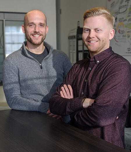 two men standing at table smiling towards camera